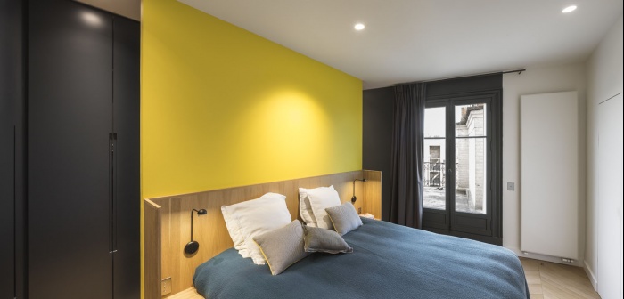Boulainvillers : Dans la chambre des parents, la tête de lit en chêne est adossée contre un mur jaune tournesol. Couleur qui se retrouve à l’intérieur des placards sur mesure, aux poignées en creux.